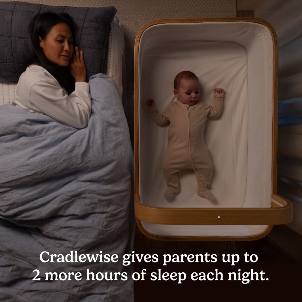 Overhead view of a baby sleeping in a Cradlewise smart crib beside their parent’s bed at night.