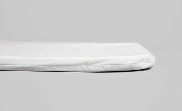 Close-up side view of the white Cradlewise crib mattress, showing its padded top and rounded, stitched edges against a light gray background.