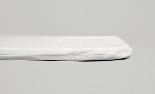 Close-up side view of the white Cradlewise crib mattress, showing its padded top and rounded, stitched edges against a light gray background.