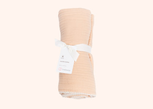 Peach Cradlewise Muslin Blanket rolled and secured with a white ribbon, with a Cradlewise product tag attached.