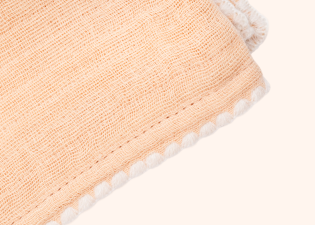 Close-up of the Peach Cradlewise Muslin Blanket, showing its crinkled organic cotton muslin texture, stitched border, and white scalloped edge.