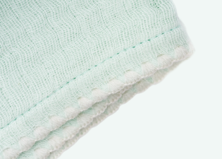 Close-up of the Mint Cradlewise Muslin Blanket, showing its crinkled organic cotton muslin texture, stitched border, and white scalloped edge.