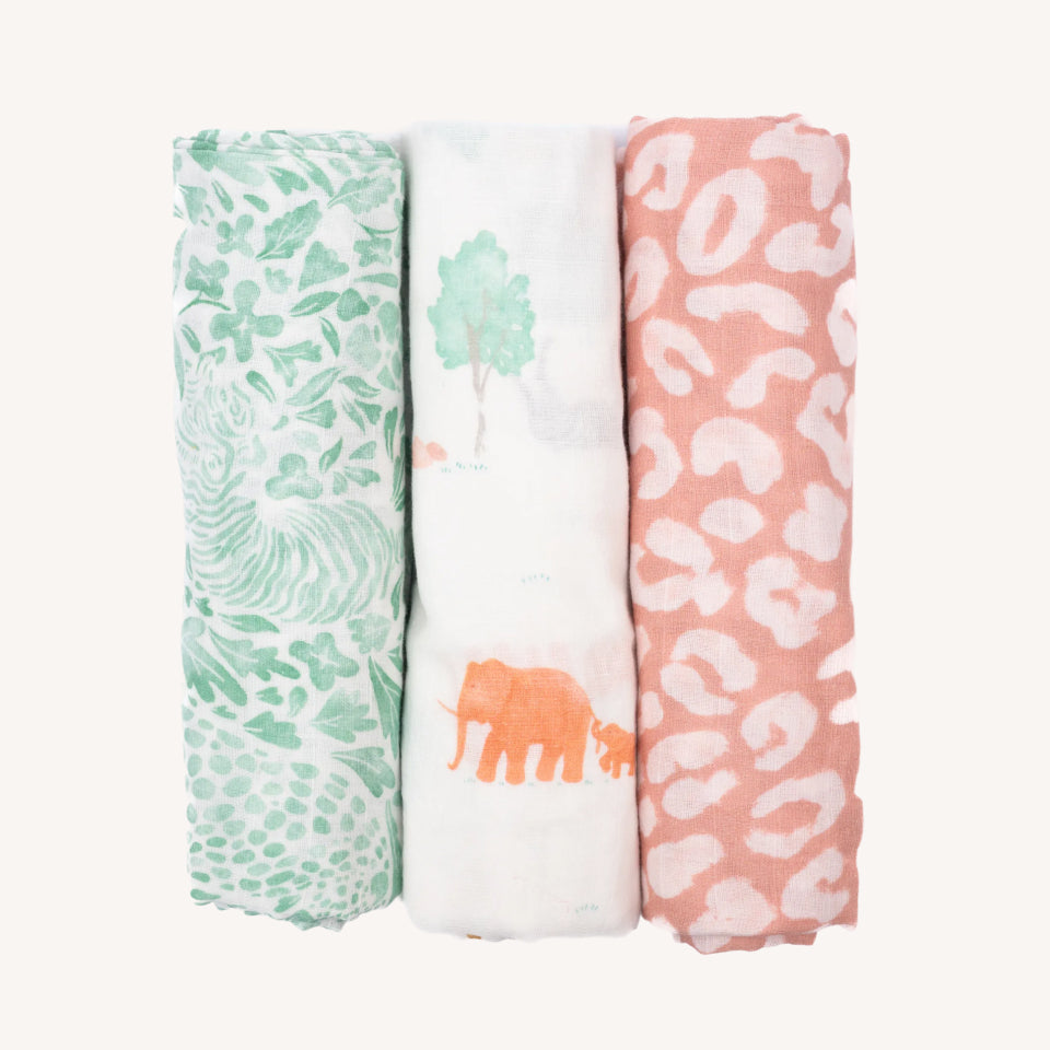 Three Cradlewise Muslin Swaddles in Jungle Safari displayed side by side, featuring a white swaddle with green tropical leaves and animal-inspired motifs, a white swaddle with watercolor safari animals and green trees, and a coral-pink swaddle with white leopard spots.