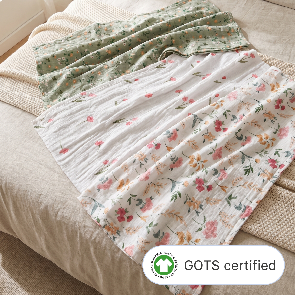 Cradlewise Muslin Swaddles in Spring Bloom draped across a bed, featuring a sage-green swaddle with small floral motifs, a white swaddle with pink flowers and green stems, and a white swaddle with pink and peach blooms, green leaves and delicate botanical branches.