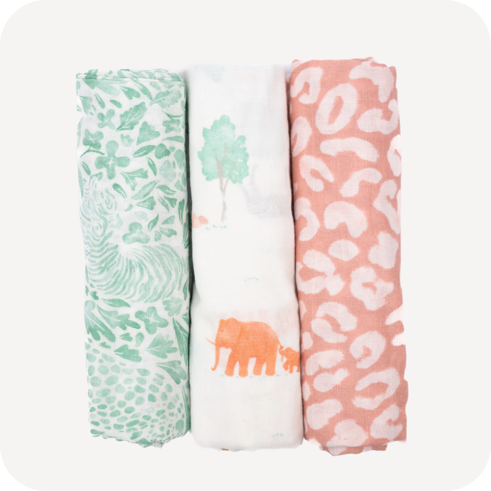 Three rolled Cradlewise Muslin Swaddles in Jungle Safari, featuring a white swaddle with green tropical leaf motifs, a white swaddle with watercolor safari animals including orange elephants and green trees, and a coral-pink swaddle with white leopard spots.